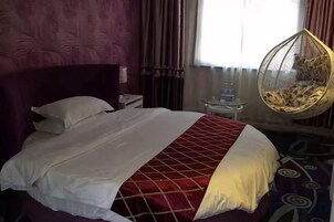A bed with a red and white bedspread, a hanging chair, and a bedside table with a lamp.