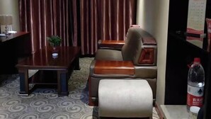Ein Hotelzimmer mit einem Holztisch, einem gepolsterten Stuhl, einem kleinen Tisch, einer Topfpflanze und einer Wasserflasche.