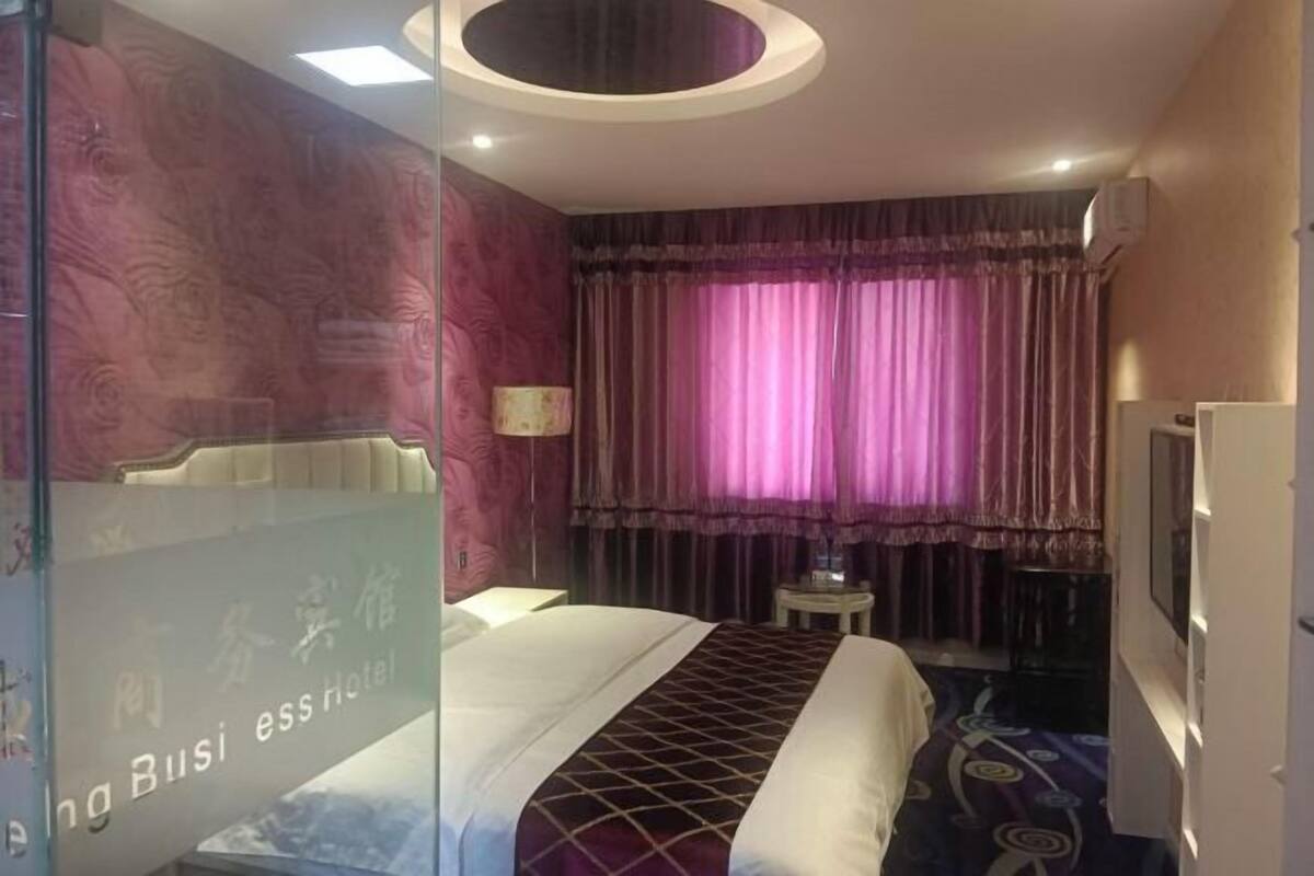 Ein Hotelzimmer mit einem Bett, einem kleinen Tisch, einer Lampe und einem Fenster mit Vorhängen.