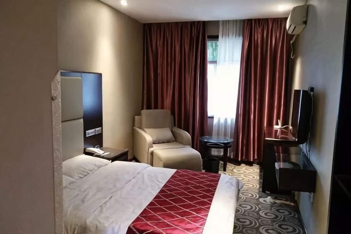 Ein Hotelzimmer mit Bett, Sessel, Schreibtisch, Fernseher und einem fensterbepflanzten Fenster.