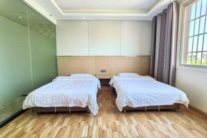 Habitación de hotel con dos camas individuales, un ventanal con cortinas, suelo de madera y un panel de vidrio en un lateral.