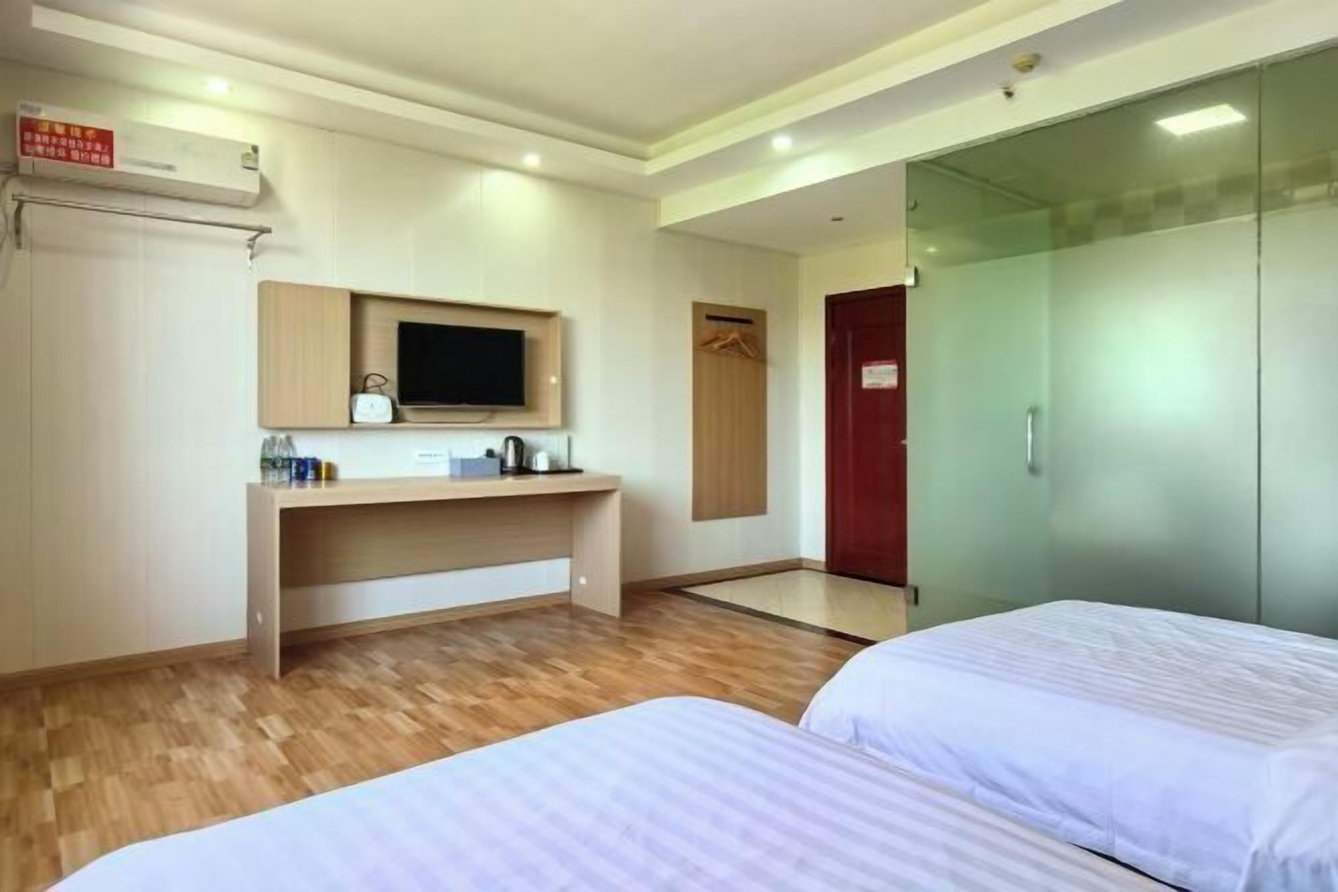 A hotel room with a bed, a desk with a TV, a wardrobe, and a glass door.