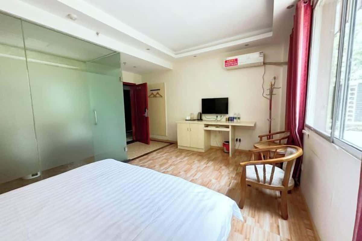 A hotel room with a bed, a desk, a chair, a television, and a window.