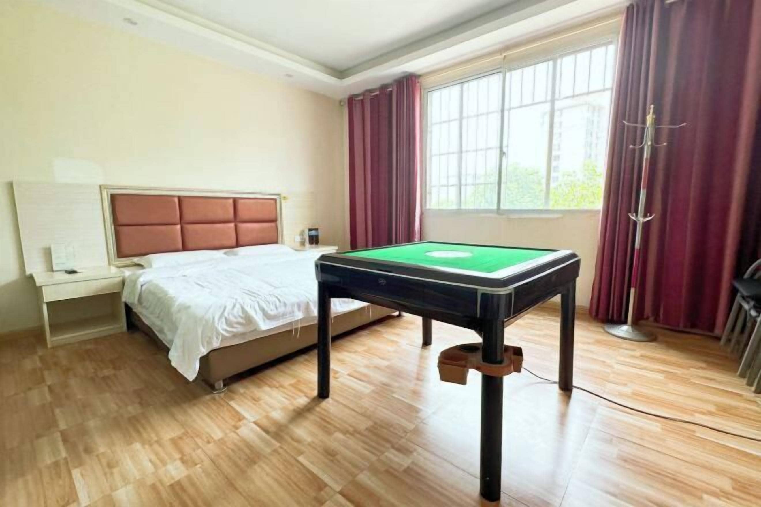 Une chambre d’hôtel avec un lit, une table de billard, une table de chevet, une lampe et une fenêtre avec des rideaux.