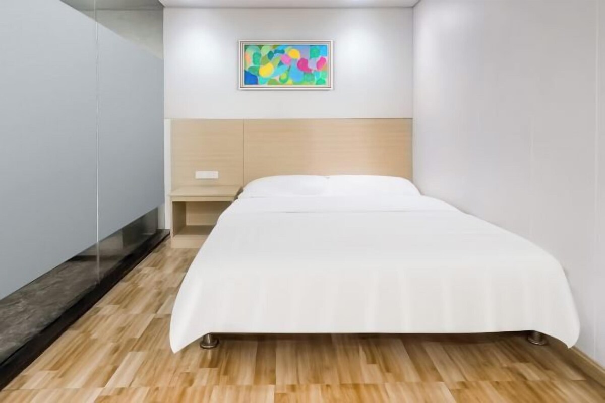 Un dormitorio moderno con una cama, un cabecero de madera, una mesita de noche pequeña y un cuadro abstracto colorido en la pared.
