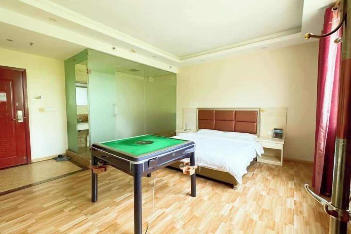 A hotel room with a bed, a small table with a green playing surface, and a mirror.