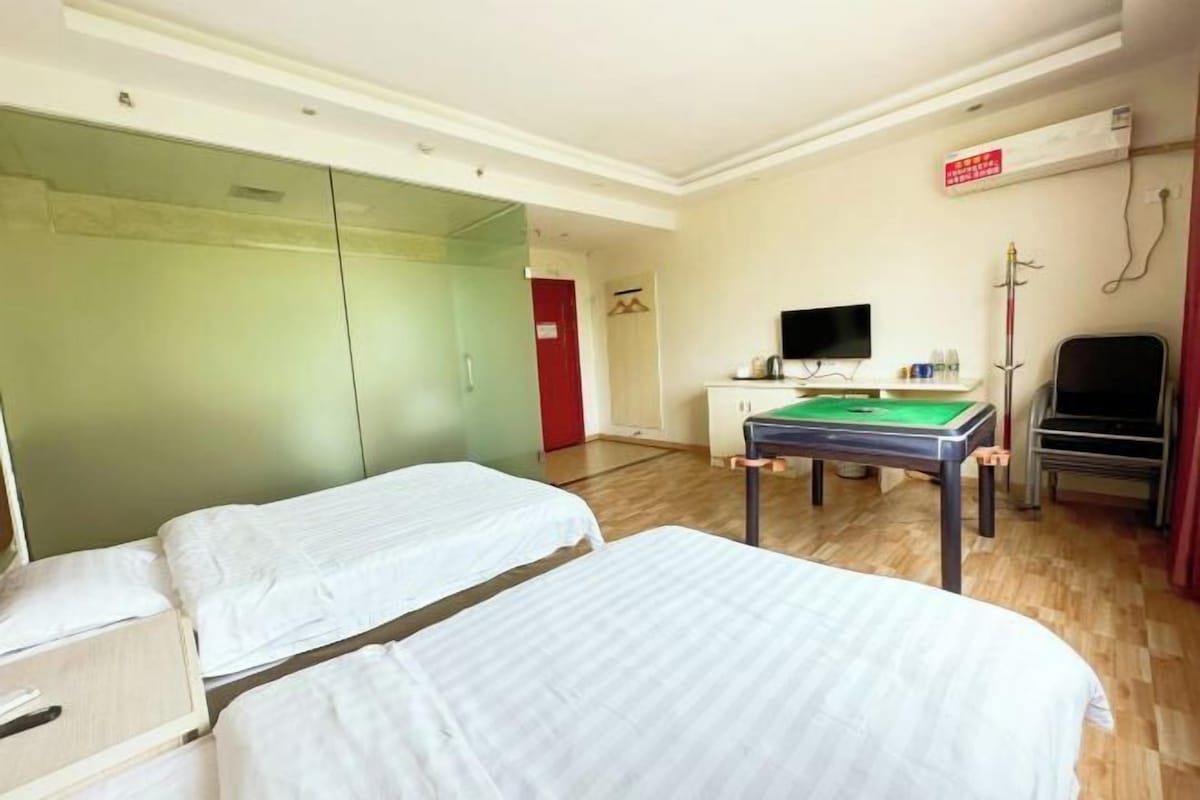 A hotel room with two beds, a desk with a television, and a green pool table.