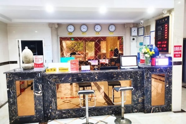 A hotel reception area with a marble counter, clocks, and a digital display.