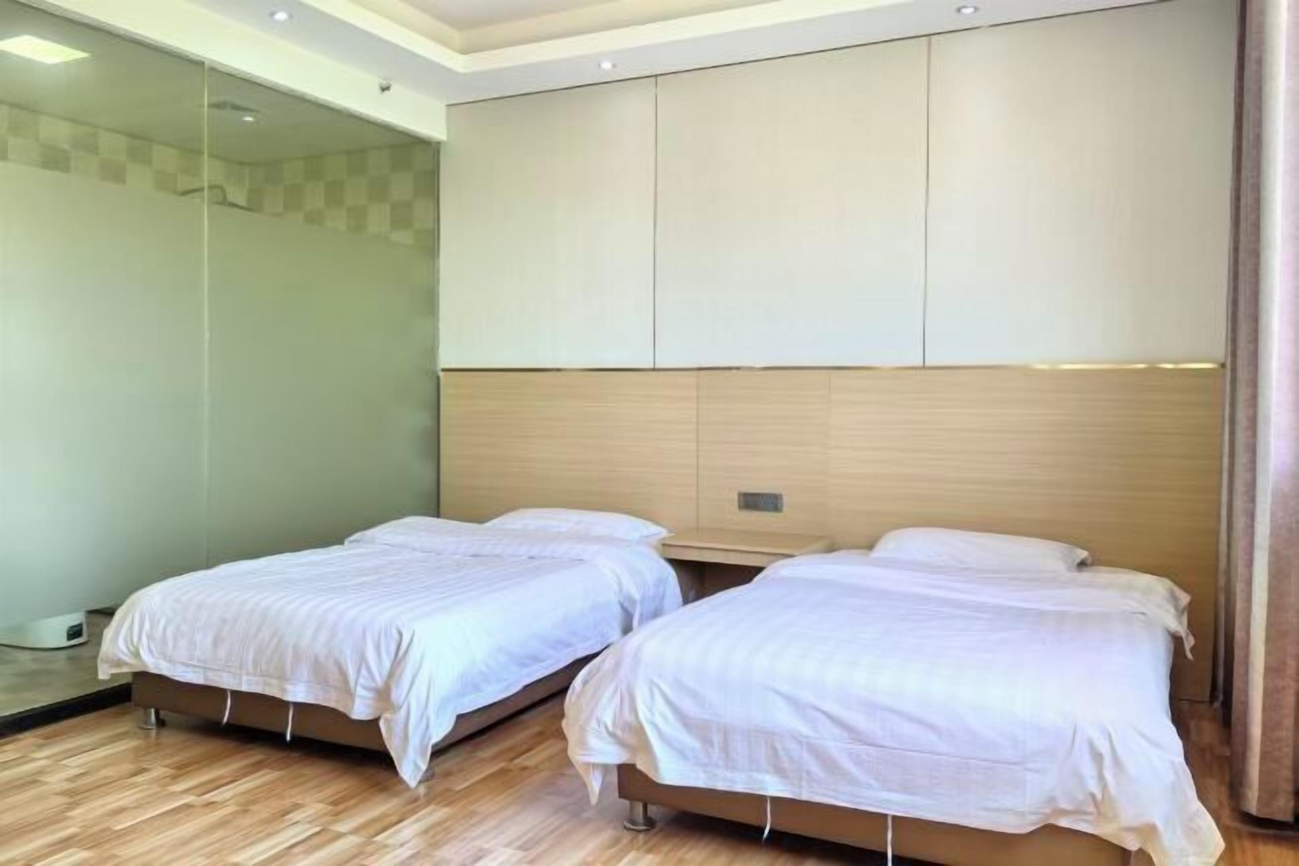 A hotel room with two single beds, a wooden headboard, and a glass shower enclosure.