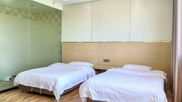 A hotel room with two single beds, a wooden headboard, and a glass shower enclosure.