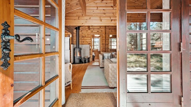 Ein Holzblockhaus-Interieur mit einem zentralen Kamin, Holzwänden und großen Fenstern.