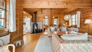 Ein Blockhaus-Interieur mit Kamin in der Mitte, Holzwänden und einer gemütlichen Sitzecke.