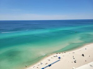 A beach with clear turquoise waters, a sandy shore, and a few beach umbrellas.