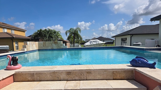 A swimming pool with steps leading into it, surrounded by houses and palm trees. - Casita Bella Beautiful Cottage IN Wonderful Cape Coral FL. Come Enjoy! (Cape Coral)
