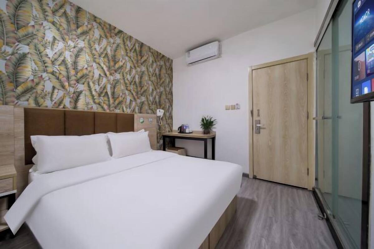 A hotel room with a bed, a wooden headboard, a small table with a plant, and a wardrobe.