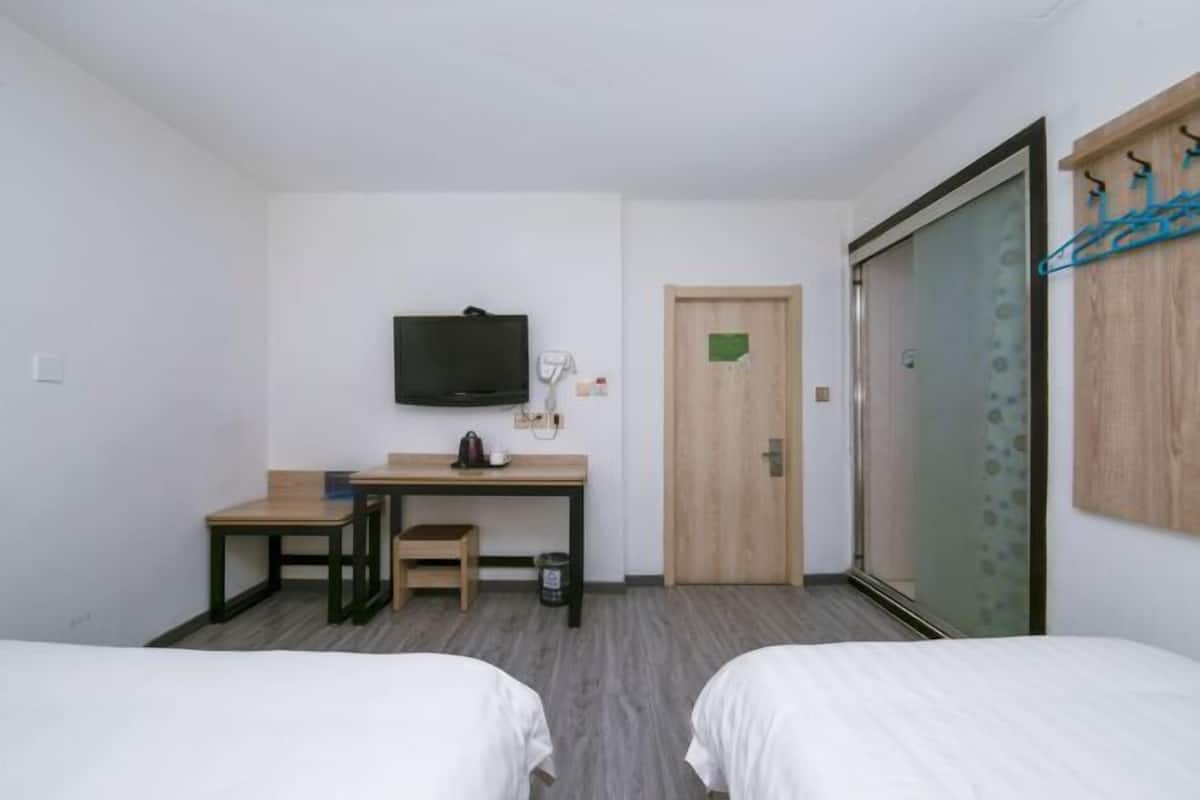 A hotel room with two beds, a desk with a chair, a television, and a sliding door.