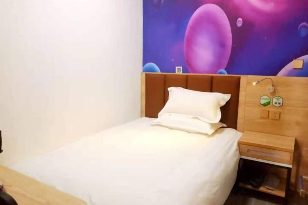 A single bed with a wooden headboard, a nightstand with a lamp, and a wall with a space-themed mural.