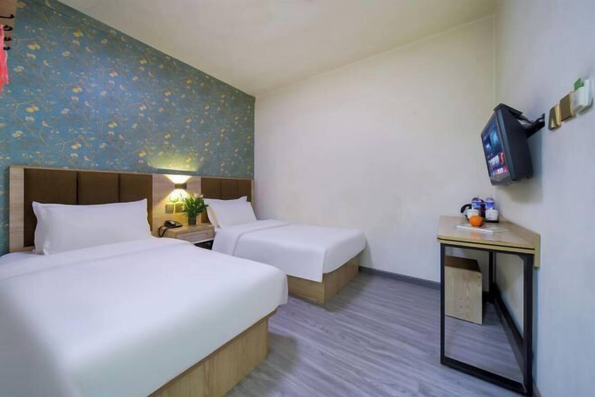 A hotel room with two beds, a small table with a TV, and a wall-mounted TV.