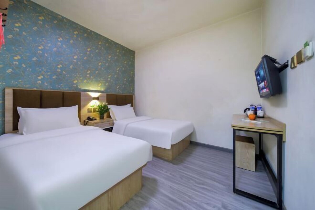 A hotel room with two beds, a small table with a TV, and a wall-mounted TV.