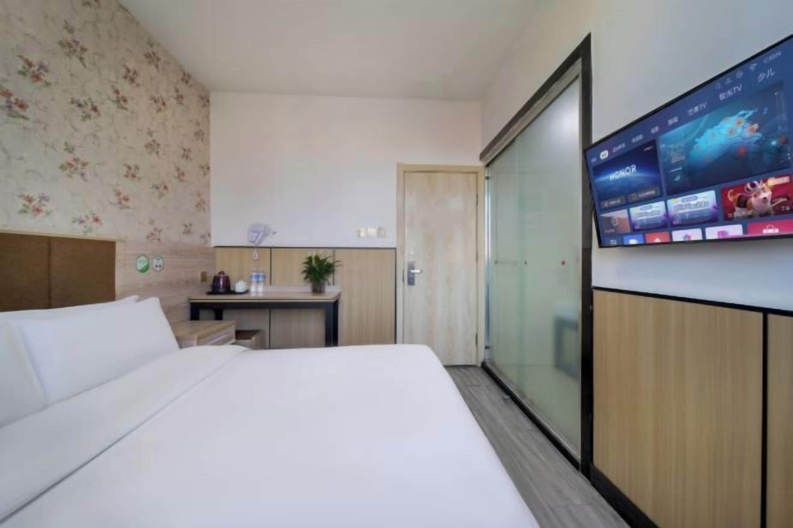Ein Hotelzimmer mit einem Bett, einem Schreibtisch, einem an der Wand montierten Fernseher und einer Schiebetür.
