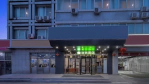 A hotel entrance with a glass facade, a green sign above the door, and air conditioning units on the exterior wall. - 99inn Selected (Beijing Huilongguan East Street Metro Station) (Beijing)