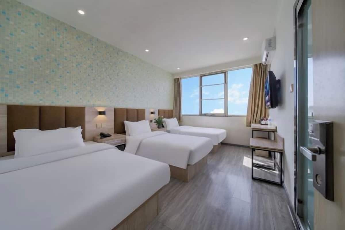 A hotel room with three beds, a TV, a desk, and a window with a view.