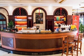 Zona de recepción de un hotel con mostrador curvo, taburetes de bar y máquina de café.