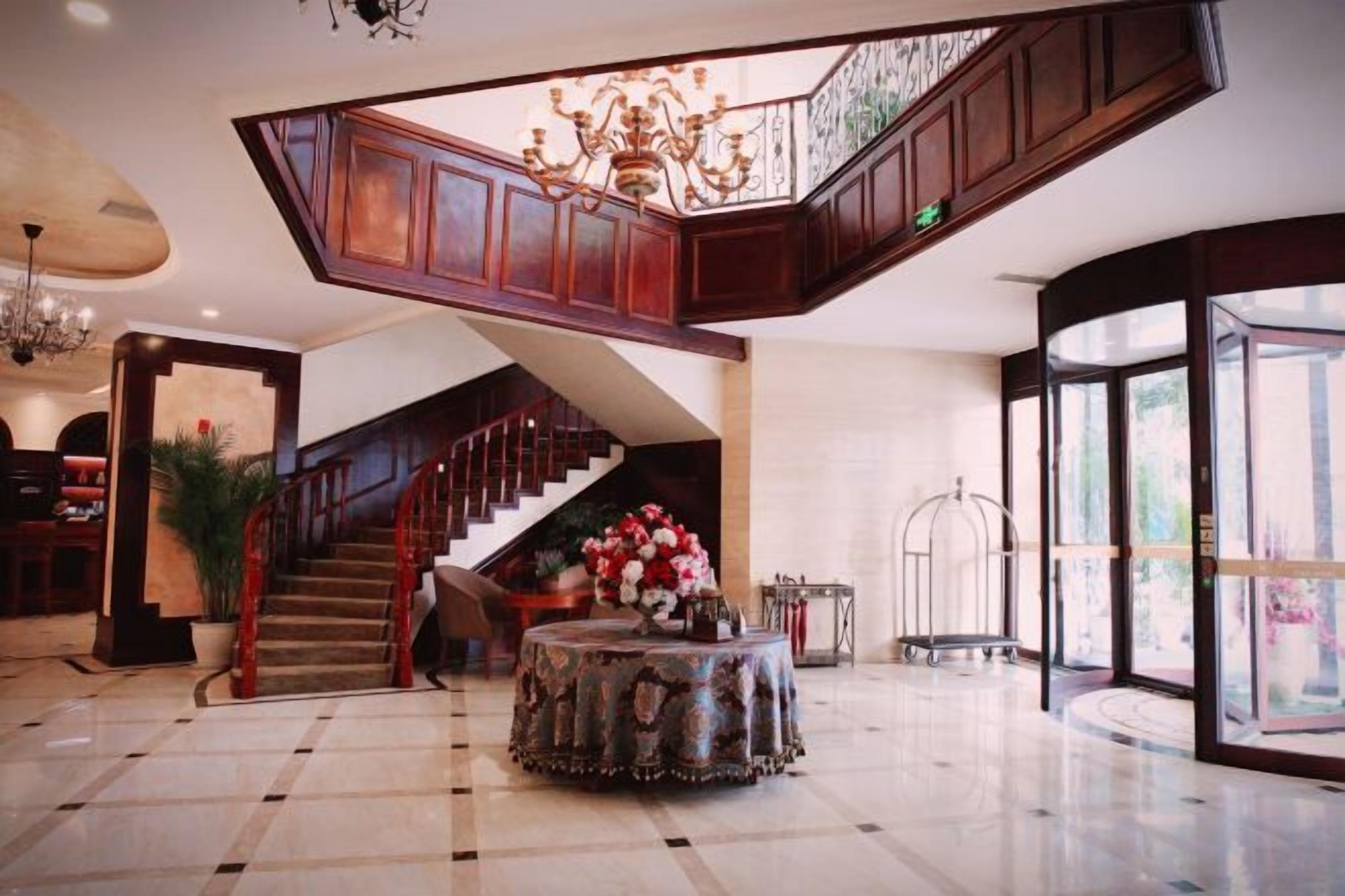 A spacious lobby with a grand staircase, a round table with flowers, and a chandelier.