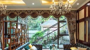 A luxurious room with a large window, a chandelier, a leather sofa, and a wooden bookshelf. - The Brilliant House (Chengdu)