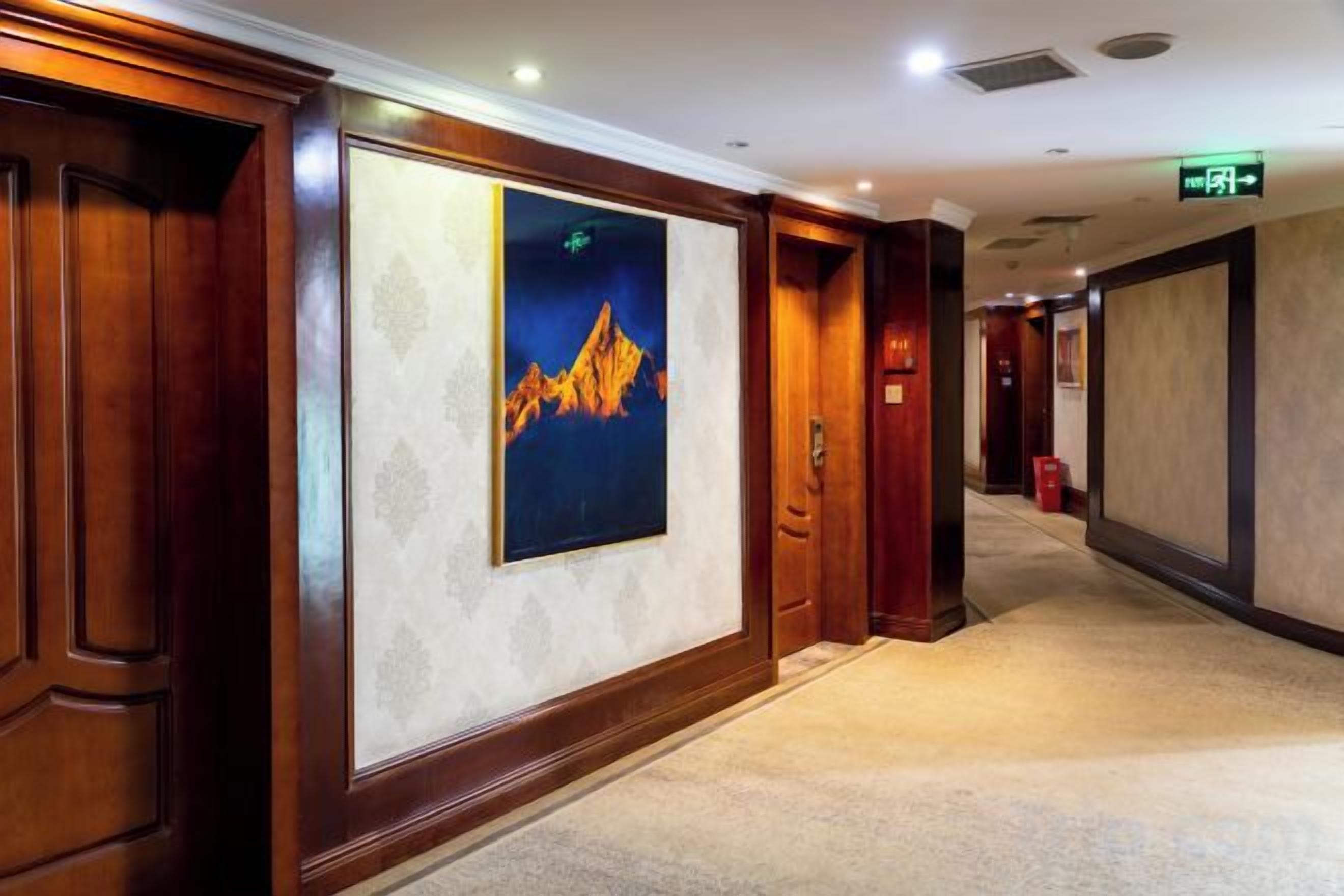 A hotel corridor with wooden paneling, a framed artwork on the wall, and a carpeted floor.