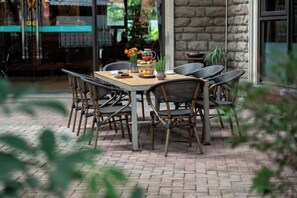 Un espacio de comedor al aire libre con suelo de ladrillo, mesa de madera y sillas de mimbre.