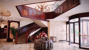 A spacious lobby with a grand staircase, a chandelier, and a round table with flowers. - The Brilliant House (Chengdu)