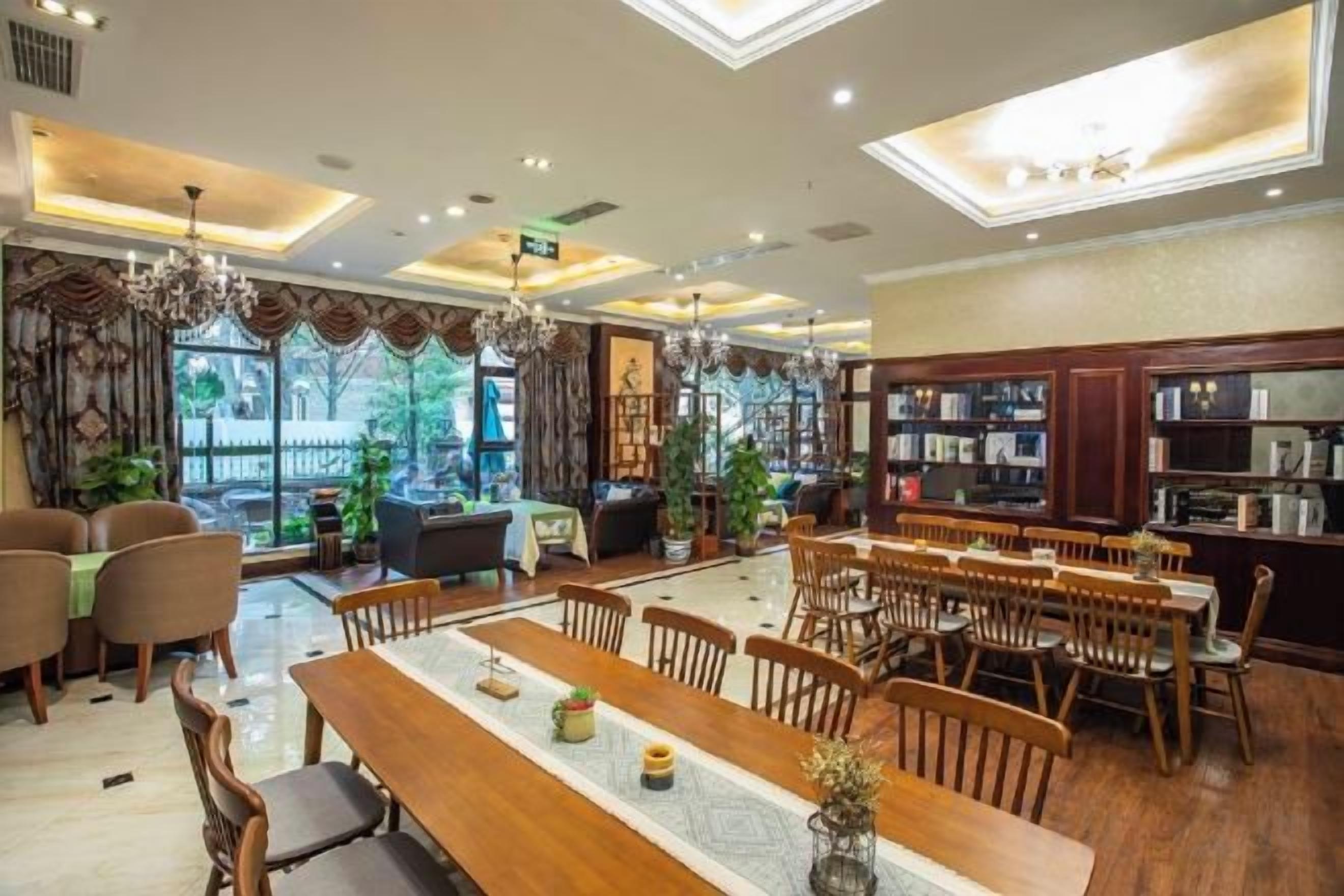 A spacious dining area with a long wooden table and multiple chairs, surrounded by bookshelves and decorative plants.