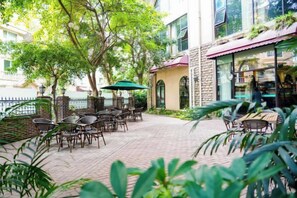 An outdoor patio with tables and chairs, surrounded by greenery and a brick pathway. - The Brilliant House (Chengdu)