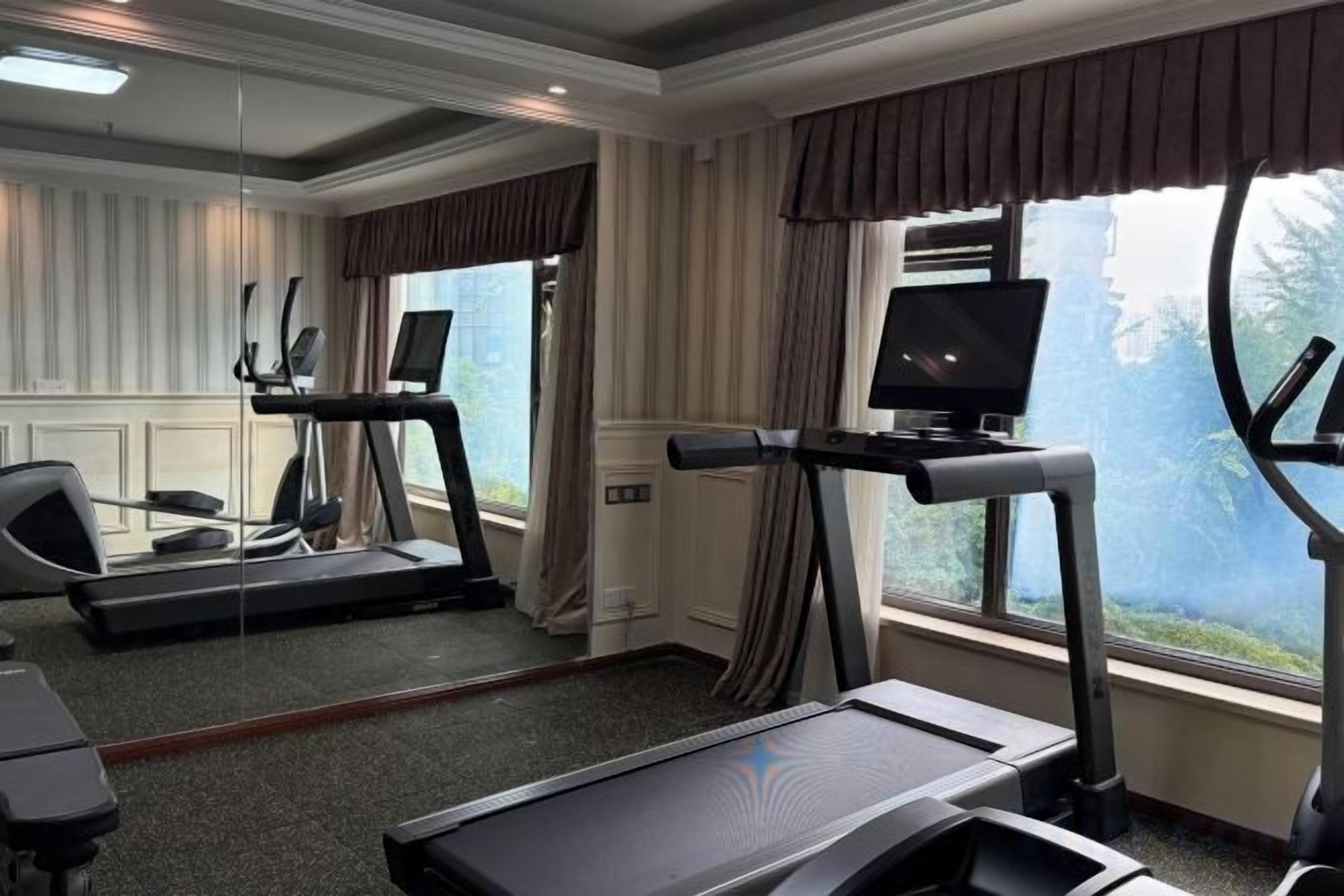 A hotel room with a treadmill, a mirror, a TV, and a window with a view.