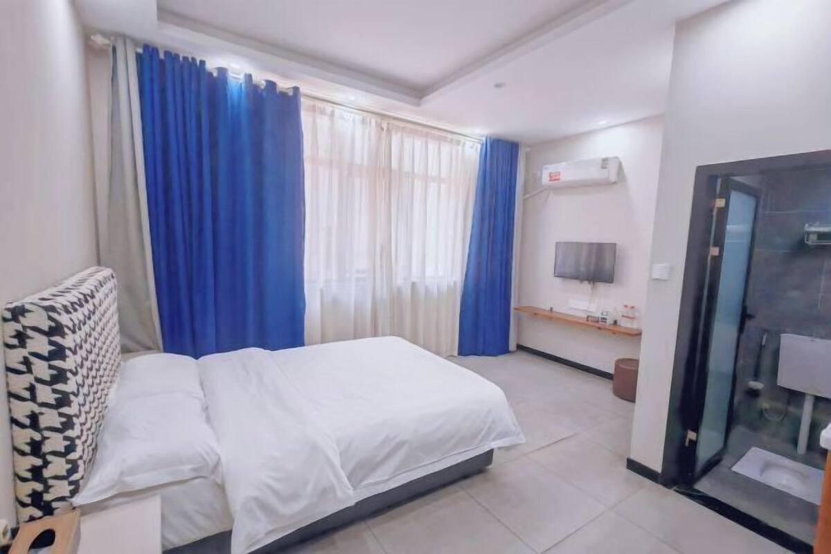 A hotel room with a bed, a TV, an air conditioning unit, and a bathroom.