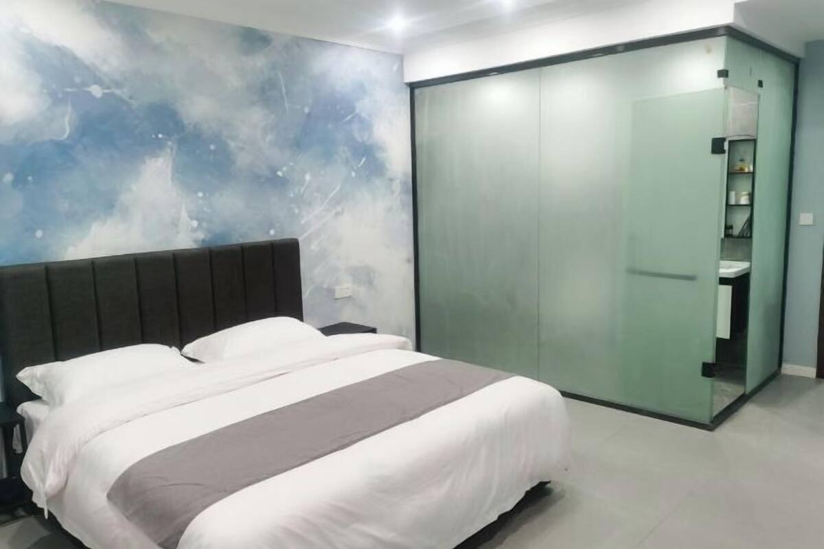 A modern bedroom with a large bed, a nightstand, a wardrobe with a mirror, and a wall with a blue abstract design.