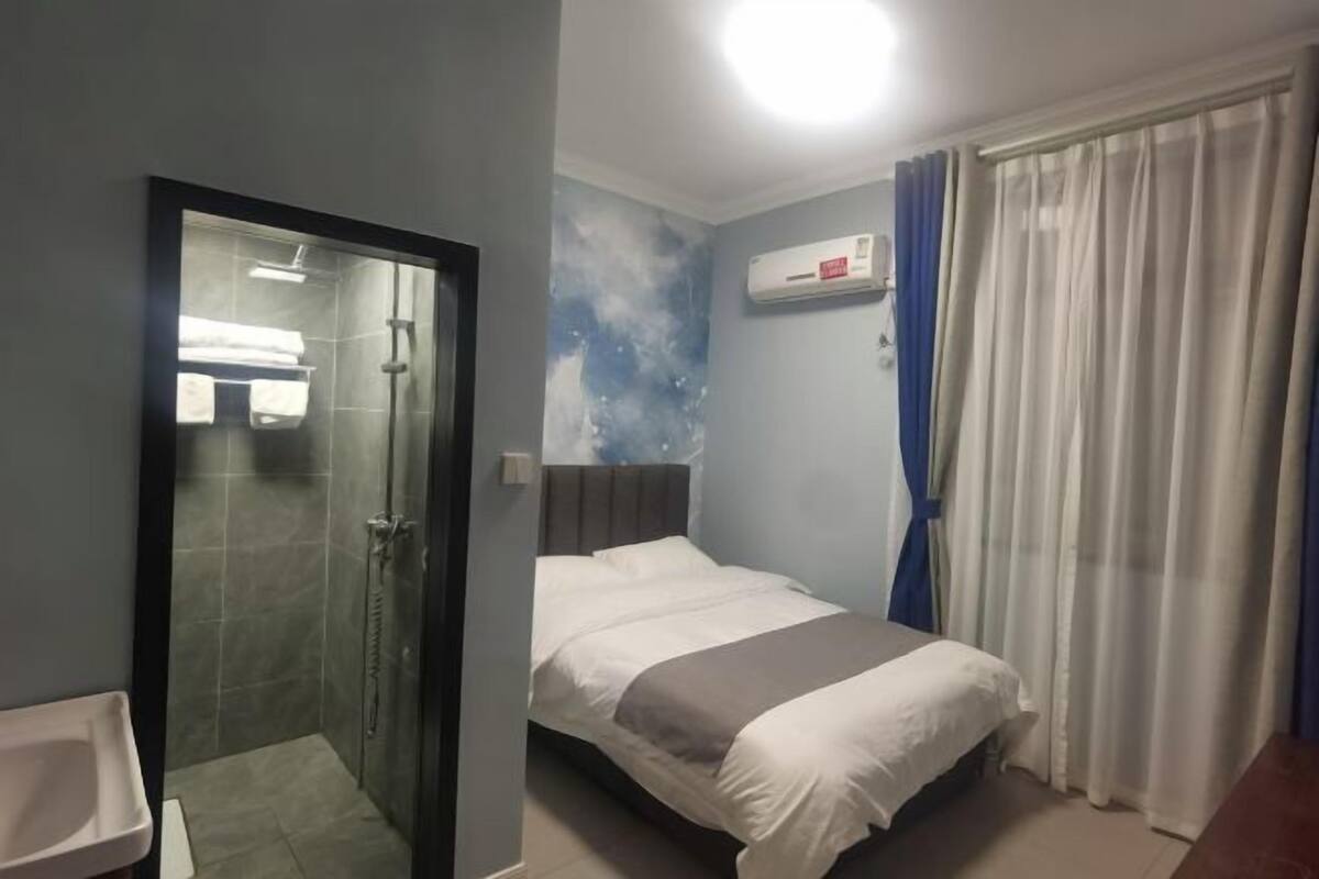 A hotel room with a bed, a shower, a sink, and a window with curtains.