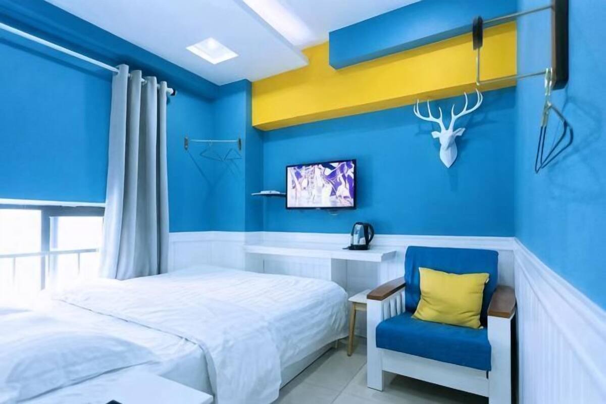 A hotel room with a bed, a desk, a chair, a television, and a wall-mounted deer head decoration.