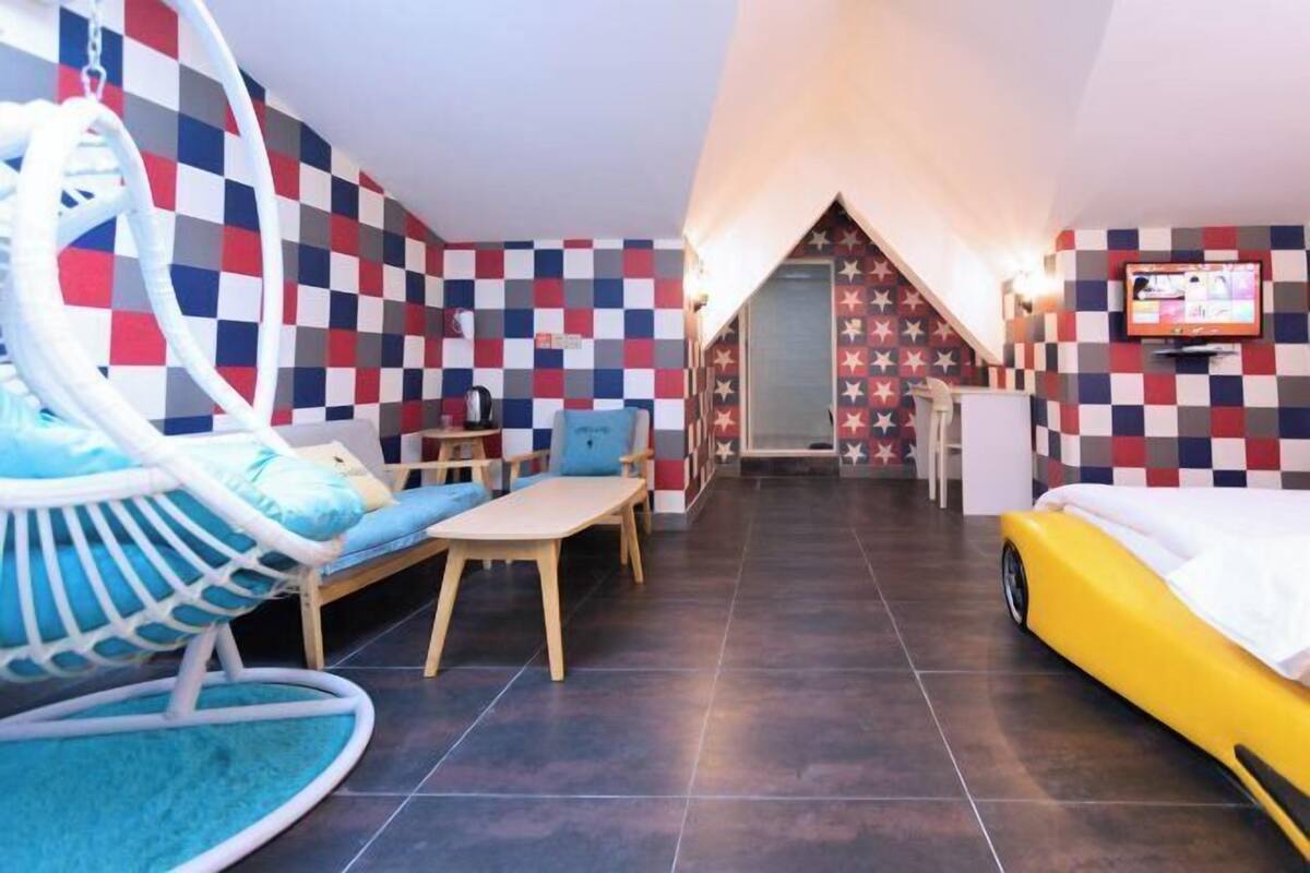 A room with a checkered wall, a hammock chair, a small table, a yellow bed, and a television.