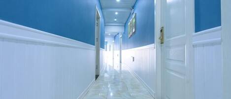 A corridor with white wainscoting and blue walls, leading to a door with a brass handle.