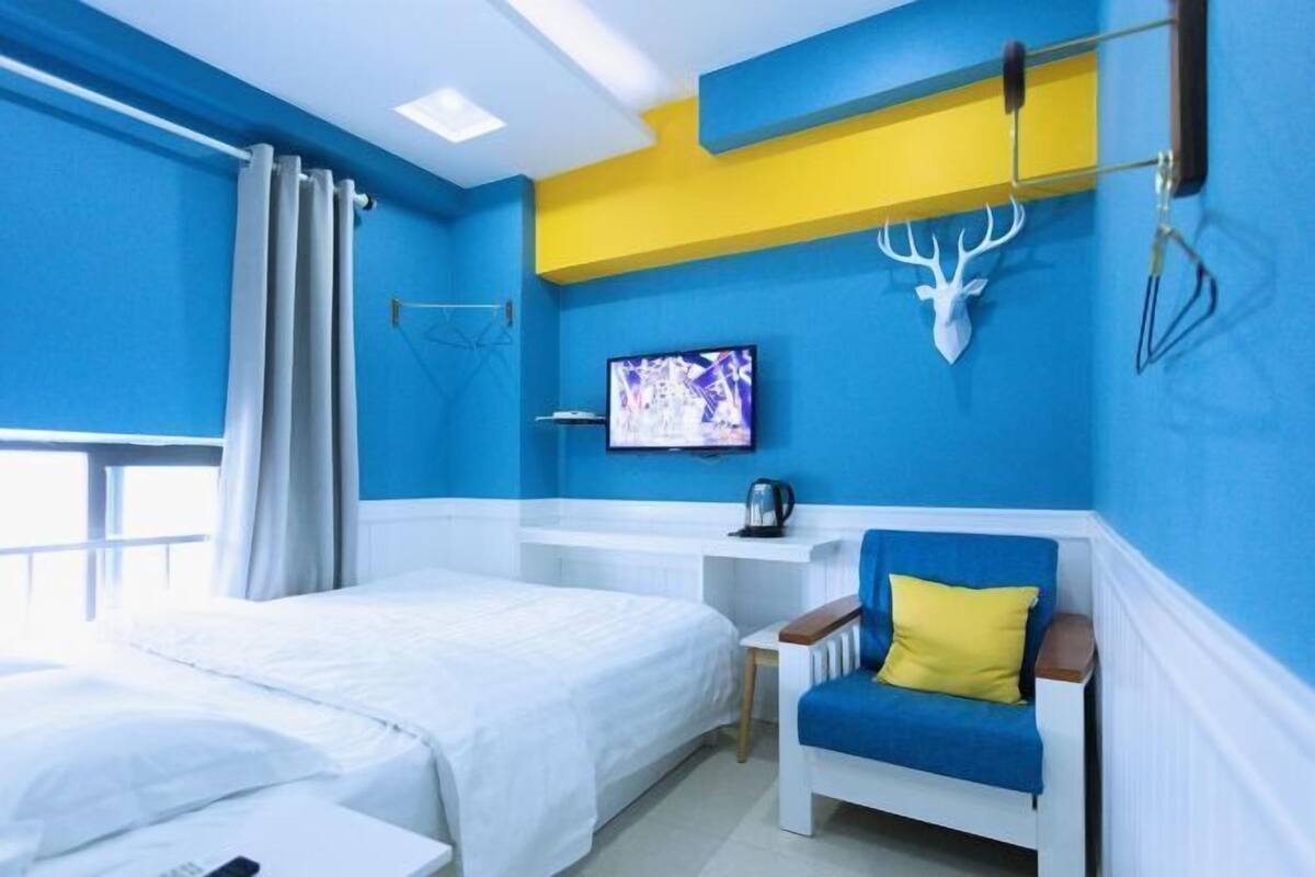 A room with a bed, a desk, a chair, a mounted deer head, a television, and a window with curtains.
