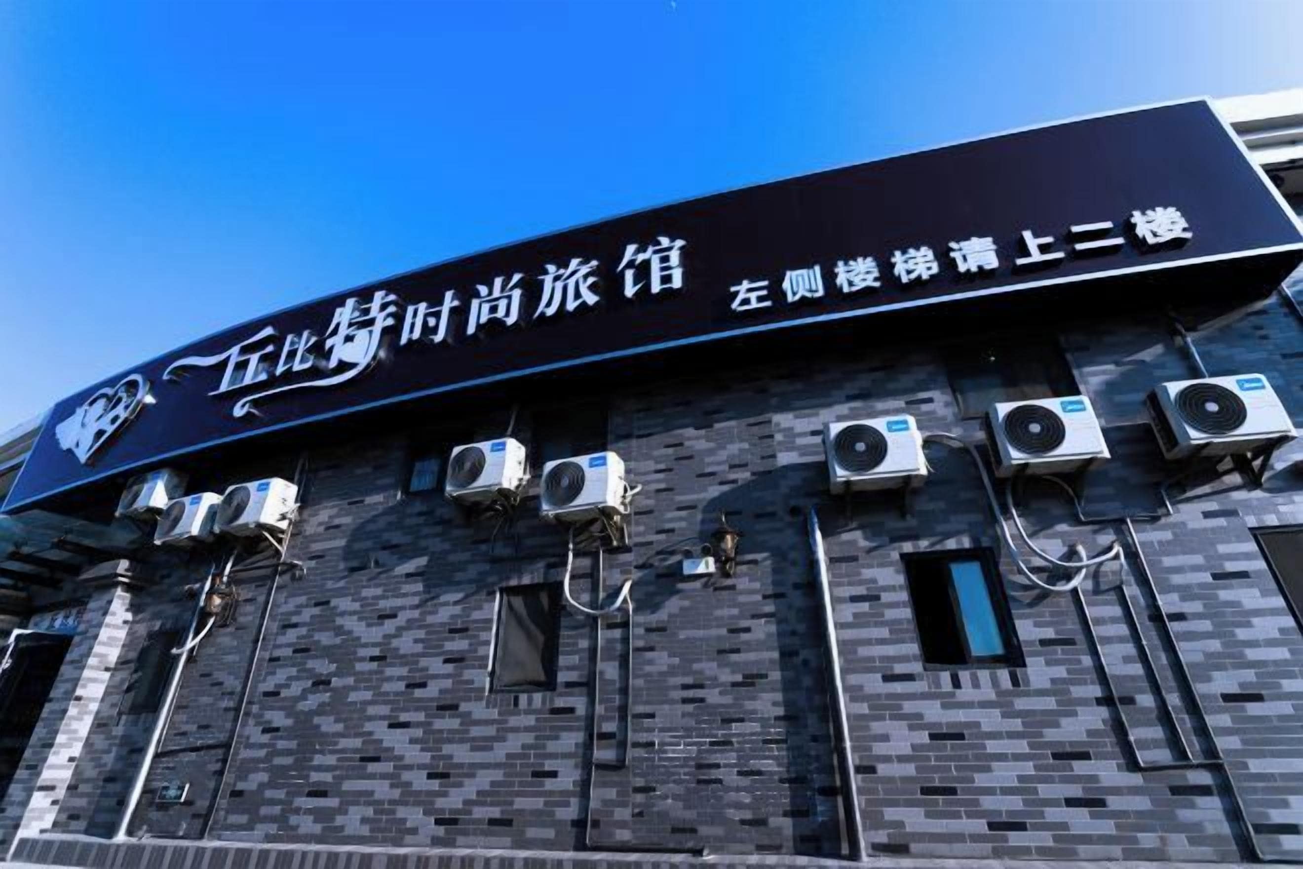 A building with a sign indicating it is a hotel. There are multiple air conditioning units attached to the exterior wall.