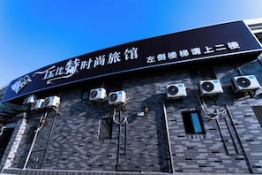 A building with a sign indicating it is a hotel. There are multiple air conditioning units attached to the exterior wall.