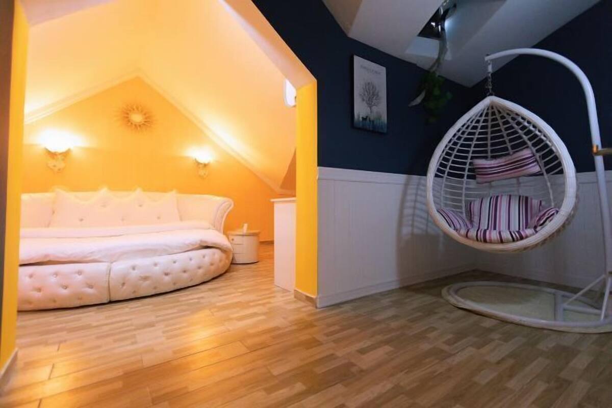 A bedroom with a bed, a hanging chair, and a ceiling light.