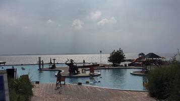 A swimming pool with a wooden deck, a lifeguard chair, and a distant view of the sea.