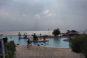 A swimming pool with a wooden deck, a lifeguard chair, and a distant view of the sea.