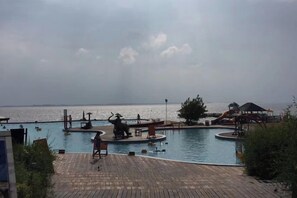 Una piscina con muelle de madera, una silla de salvavidas y vista al mar en la distancia.