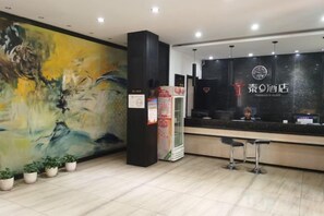 Zona de recepción de hotel con un cuadro abstracto grande, un mostrador de recepción y un mostrador con un logotipo.