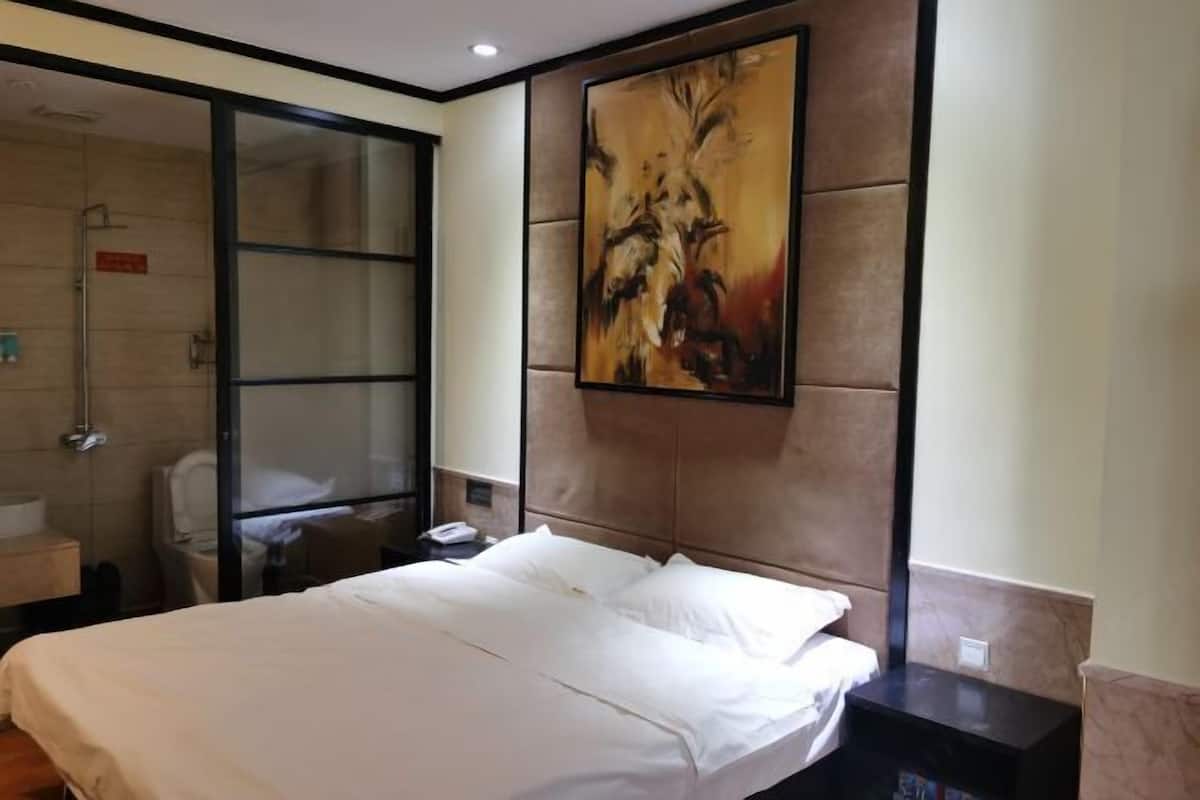 A hotel room with a large bed, a glass shower enclosure, and a painting on the wall.